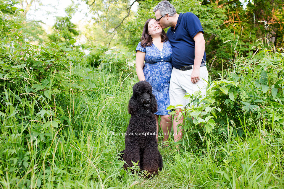 Cute couple snuggles while black poodle looks on at pet photography session at Ontario park.